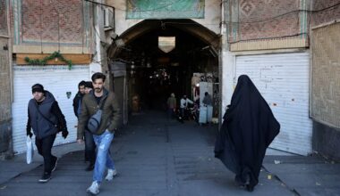 Shops with metal shutters closed as people walk past the entrance of the Tehran Grand Bazaar.