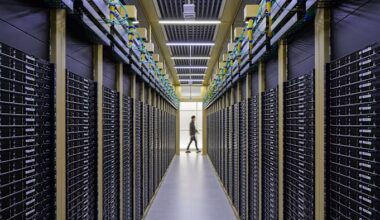 Rows of black server racks line a corridor in the Naver Data Center at GAK Chuncheon, with a person walking in the distance