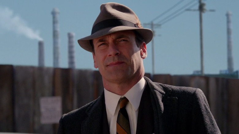 Don Draper, wearing a suit and hat, stands outdoors in 