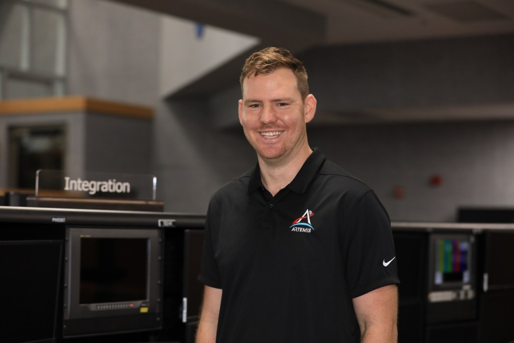 Image shows man smiling in black shirt with NASA's Artemis logo.