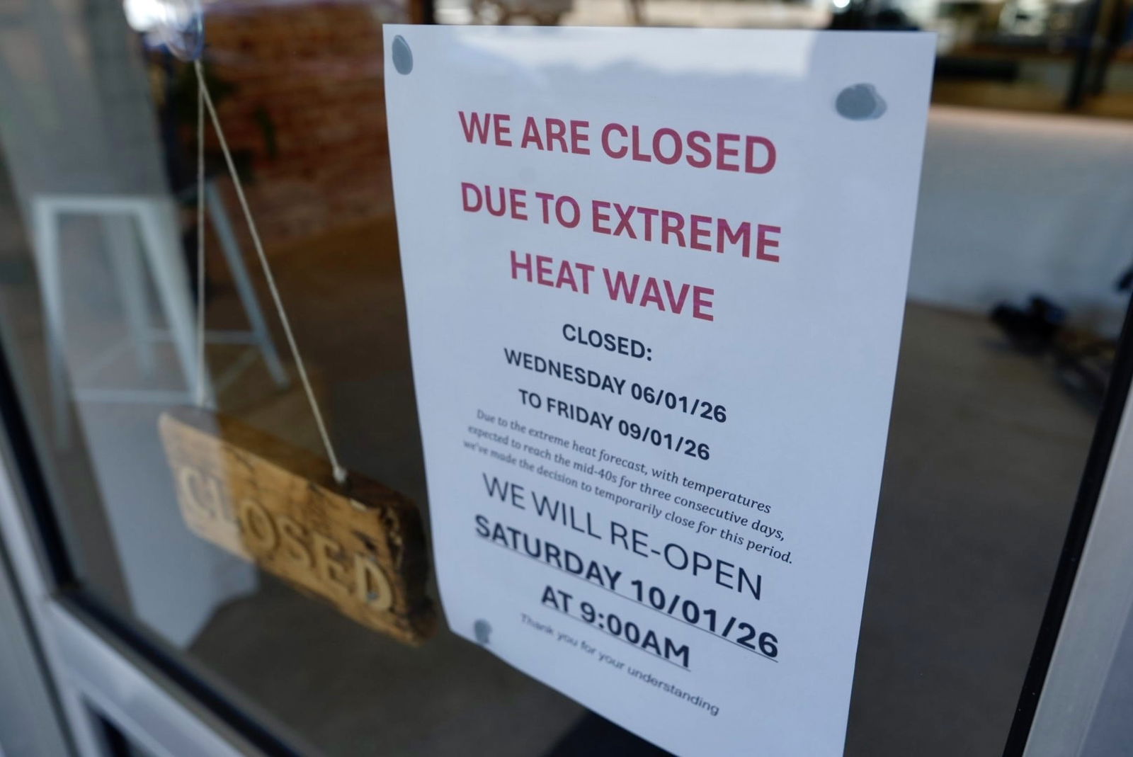 A sign on the door of a shop saying the store is closed due to extreme heatwave.