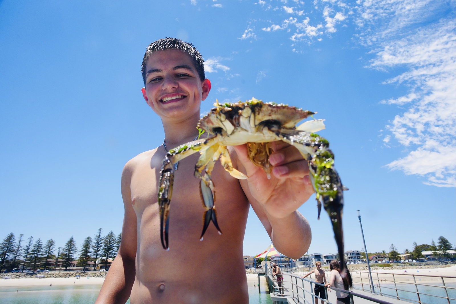 A smiling teenage boy holds a crab up to the camera. 