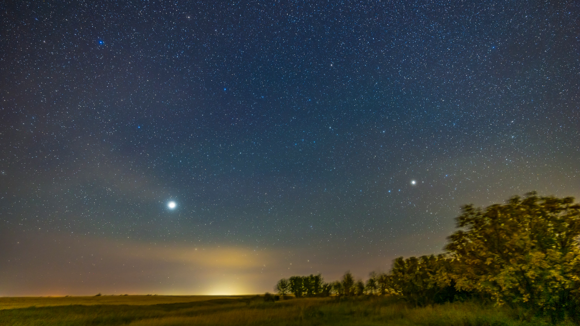 A blue and yellow night sky glows over a forested green landscape with a bright dot in the center of the image.