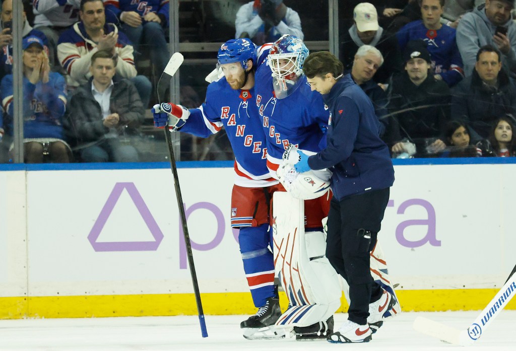 New York Rangers goaltender Igor Shesterkin is helped off the ice by a trainer and defenseman Vladislav Gavrikov.