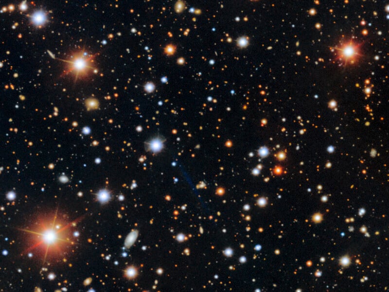 A deep field image of space showing countless stars and distant galaxies of various colors and brightnesses scattered across a dark background. Some stars have noticeable diffraction spikes.