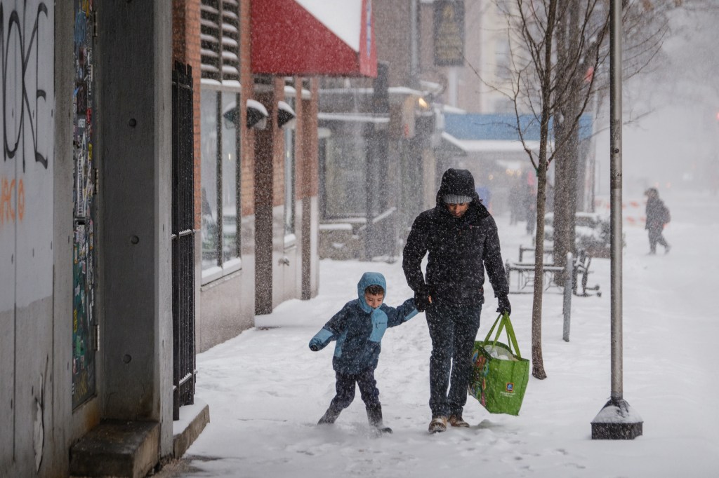 A man and child walk down a snow-covered street during a snowstorm in New York City.