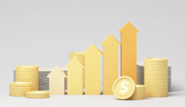 Gold colored arrows pointing upwards in a row and increasing in height with coins stacked next to them depicting a bull market, positive financial gains