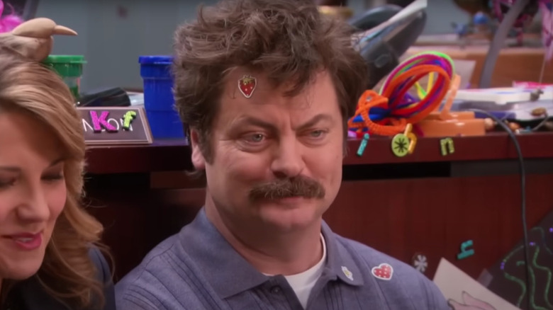 Nick Offerman's Ron Swanson with messy hair and a strawberry sticker stuck on his forehead on Parks and Recreation