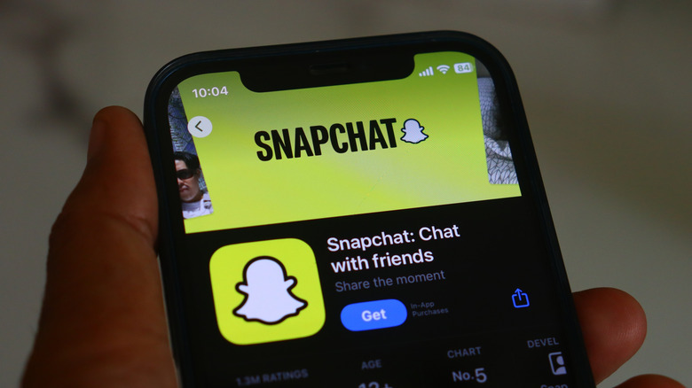 Hand holding a phone displaying Snapchat's App Store listing