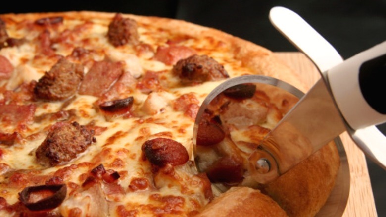 A pizza slicer cutting up a meat lover's pizza