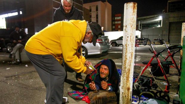 Stan Levin, left, kneels down to give Shayne Dunn, who is homeless, a package of food, as part of his volunteer work for San Diego Veterans for Peace in downtown San Diego on Dec. 29, 2017. Hayne Palmour IV / U-T File