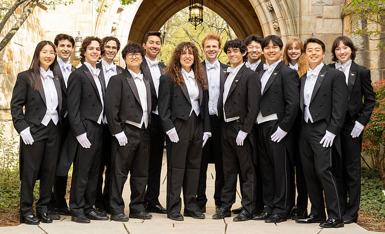 Singing group in formal dress standing in front of stone gateway.