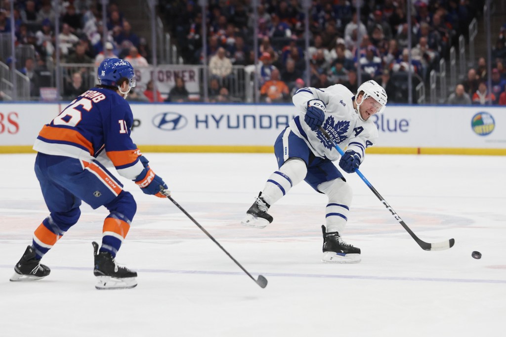 Toronto Maple Leafs' Morgan Rielly, right, passes the puck around New York Islanders' Marc Gatcomb during the first period of an NHL hockey game, Saturday, Jan. 3, 2026.