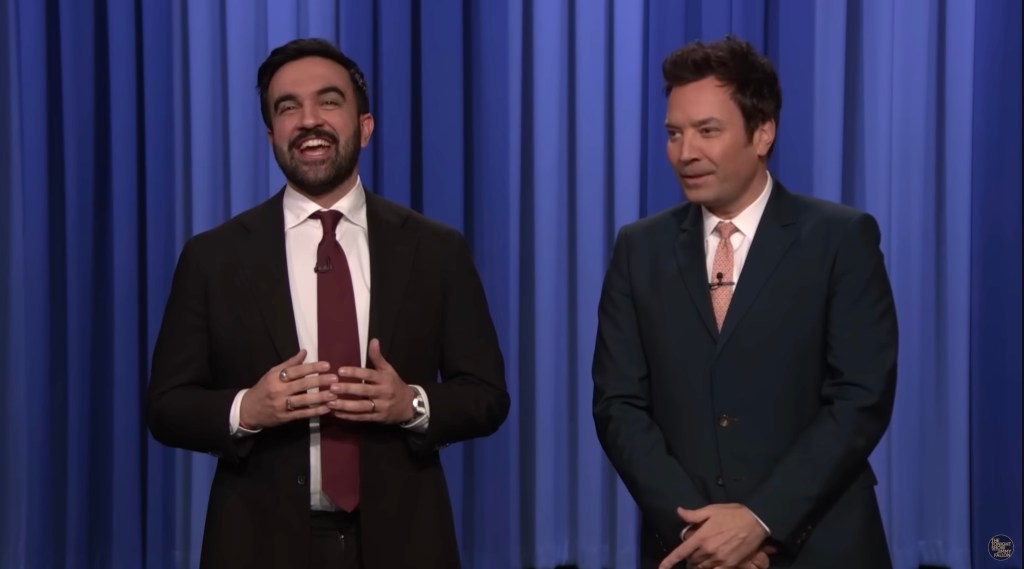 Zohran Mamdani and Jimmy Fallon on stage in front of a blue curtain.