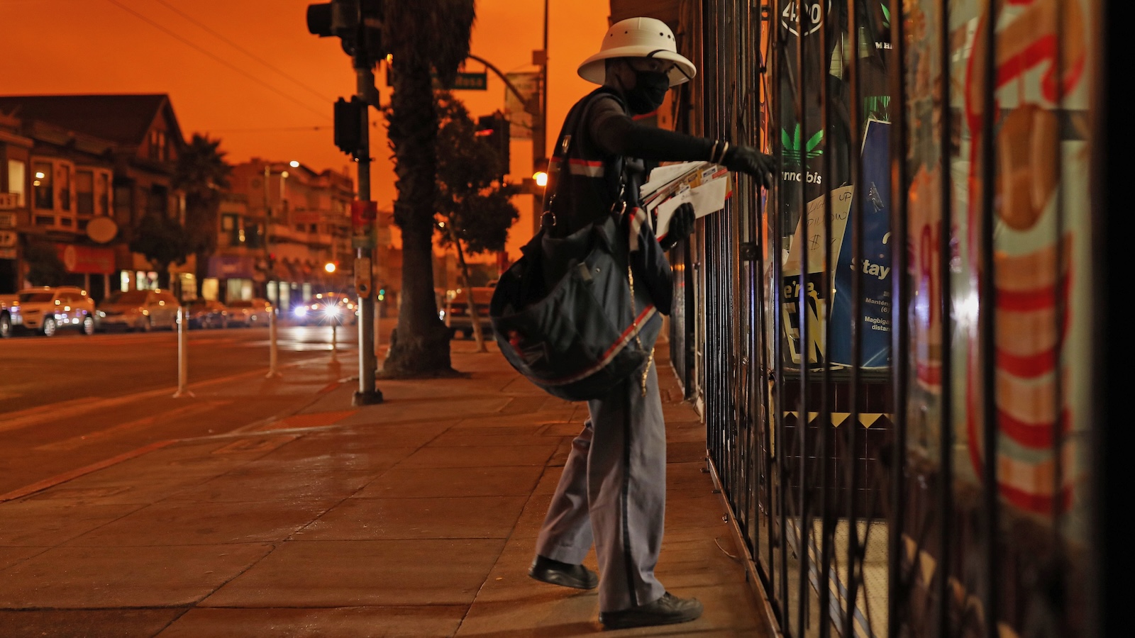 A postal carrier makes deliveries in San Francisco, the mid-day sky darkened and orange from smoke wafting in from wildfires burning hundres of miles away.