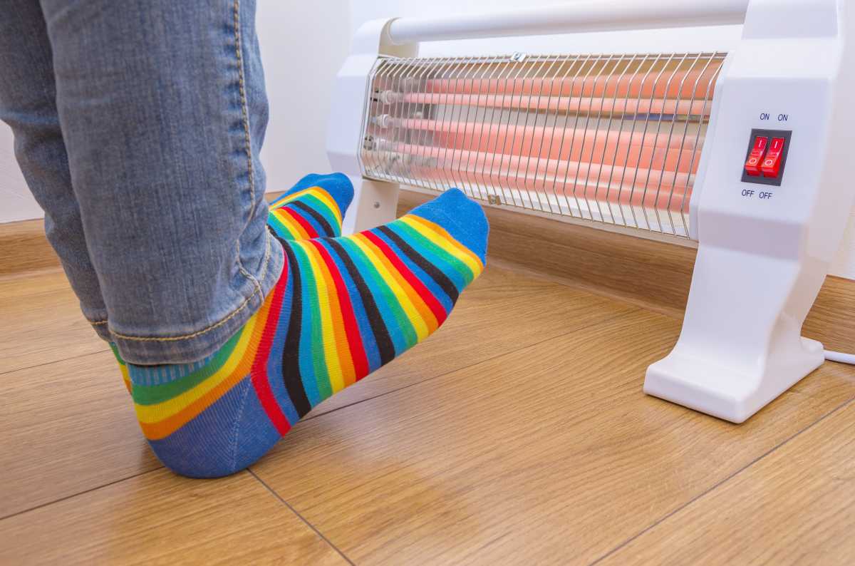 A person wearing bright rainbow-colored socks and warms cold feet near an electric space heater in winter. Infrared halogen heater at home.