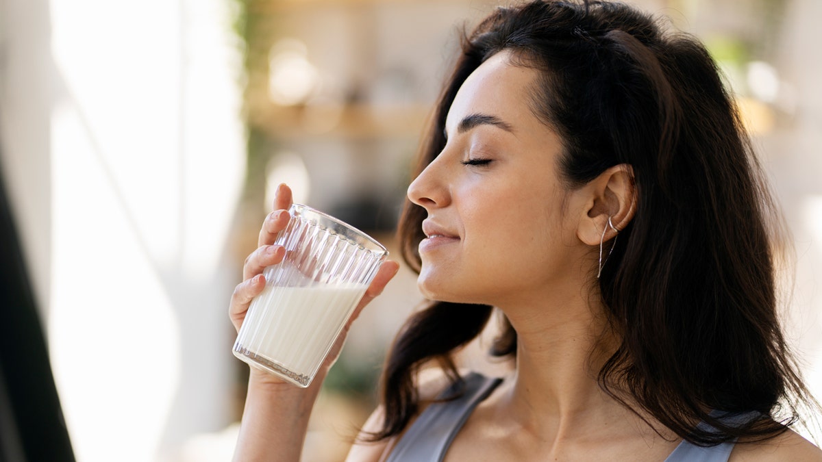 A woman drinks a glass of milk with her eyes closed.