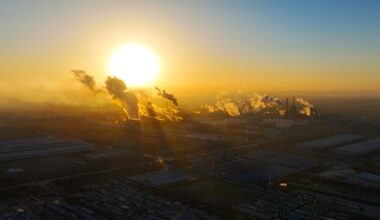 A large, yellow sun is pictured shining close to the horizon over an industrial region of China as smoke from industry pours into the air to reflect the light.