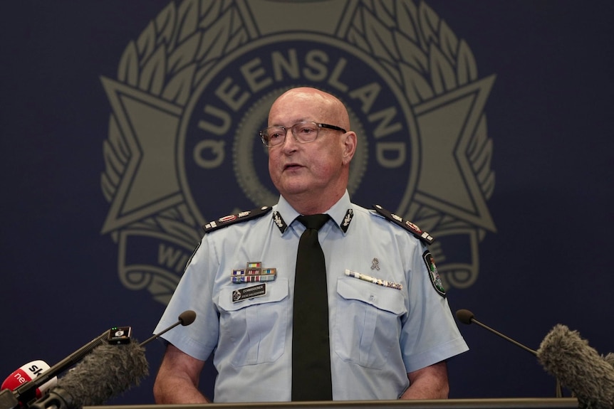Steve Gollschewski stands behind a microphe with the Queensland police logo behind him.