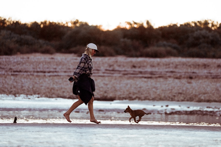 a woman walking on the beach with a baby dingo