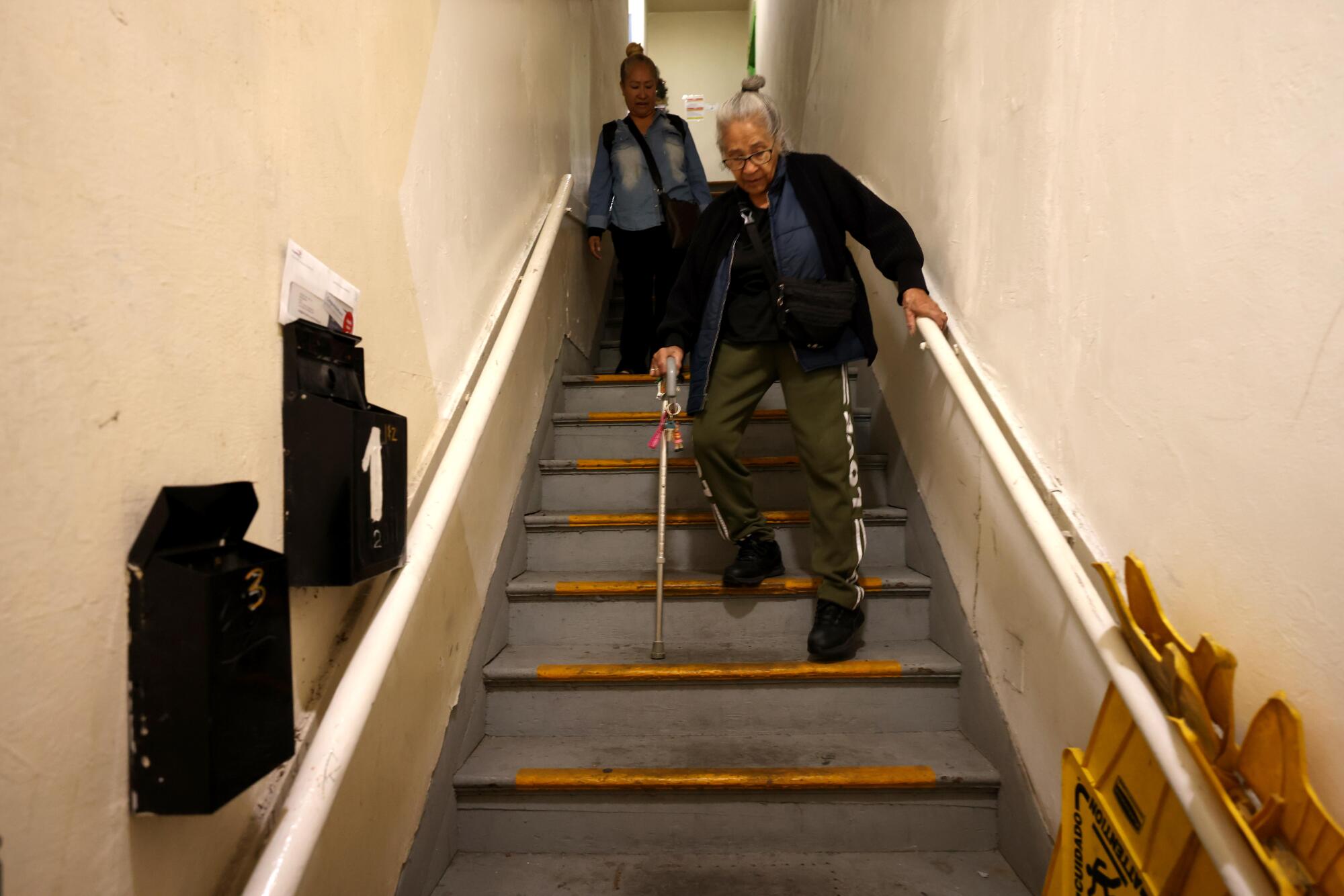 A woman uses a cane to walk down a staircase.