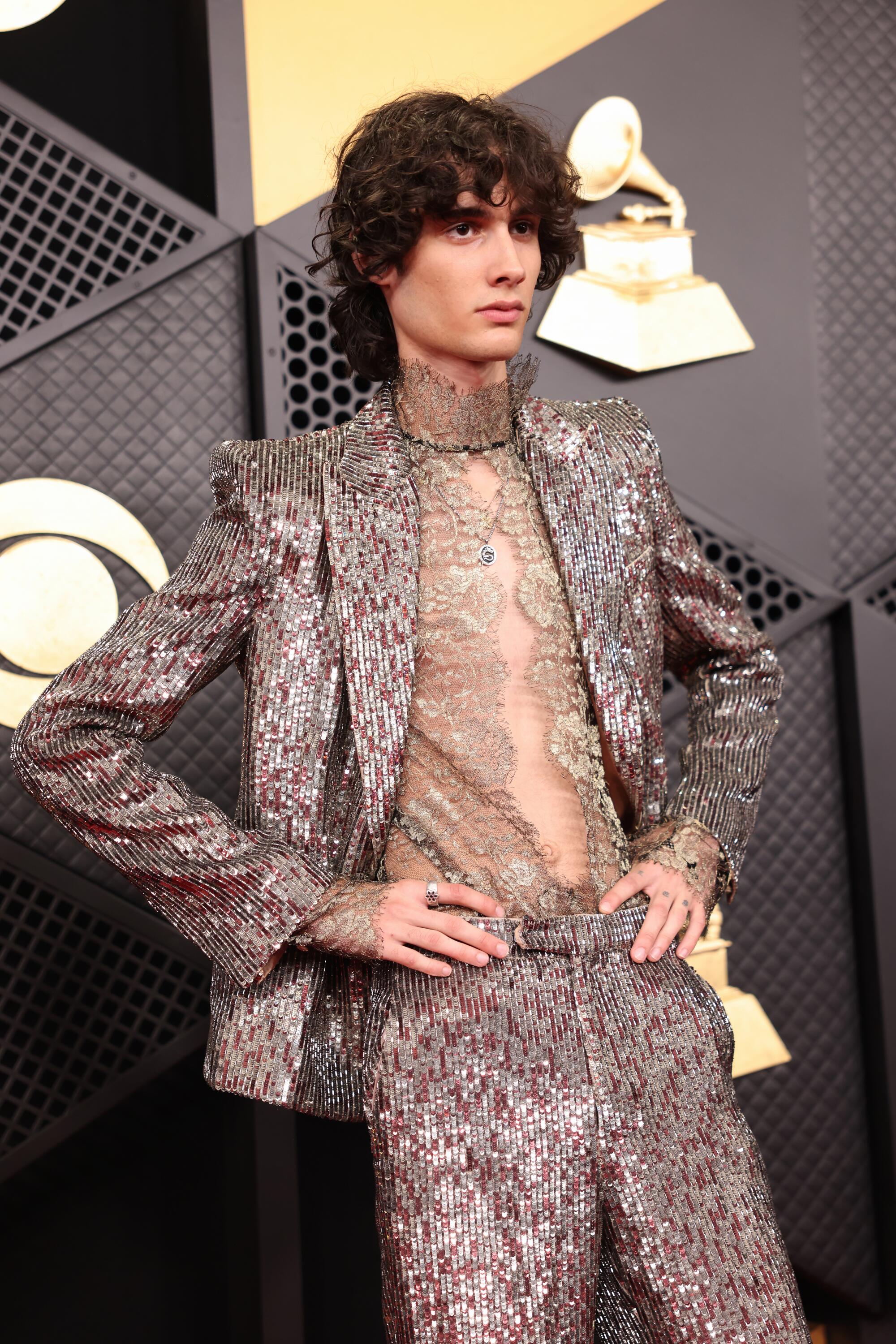 Sombr, wearing a sequined suit, rests his hands on his hips. 