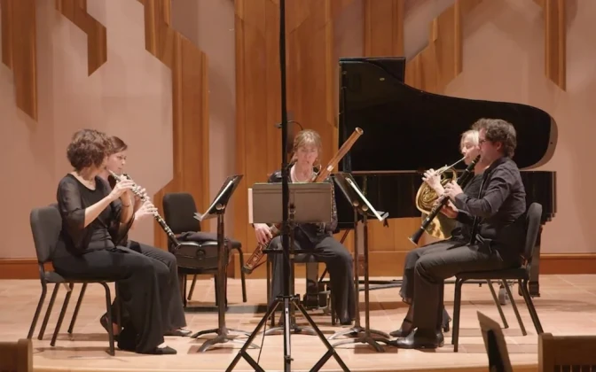 A woodwind quintet featuring four light-skinned women and one light-skinned man. There's a flute, an oboe, a bassoon, a french horn and a clarinet.