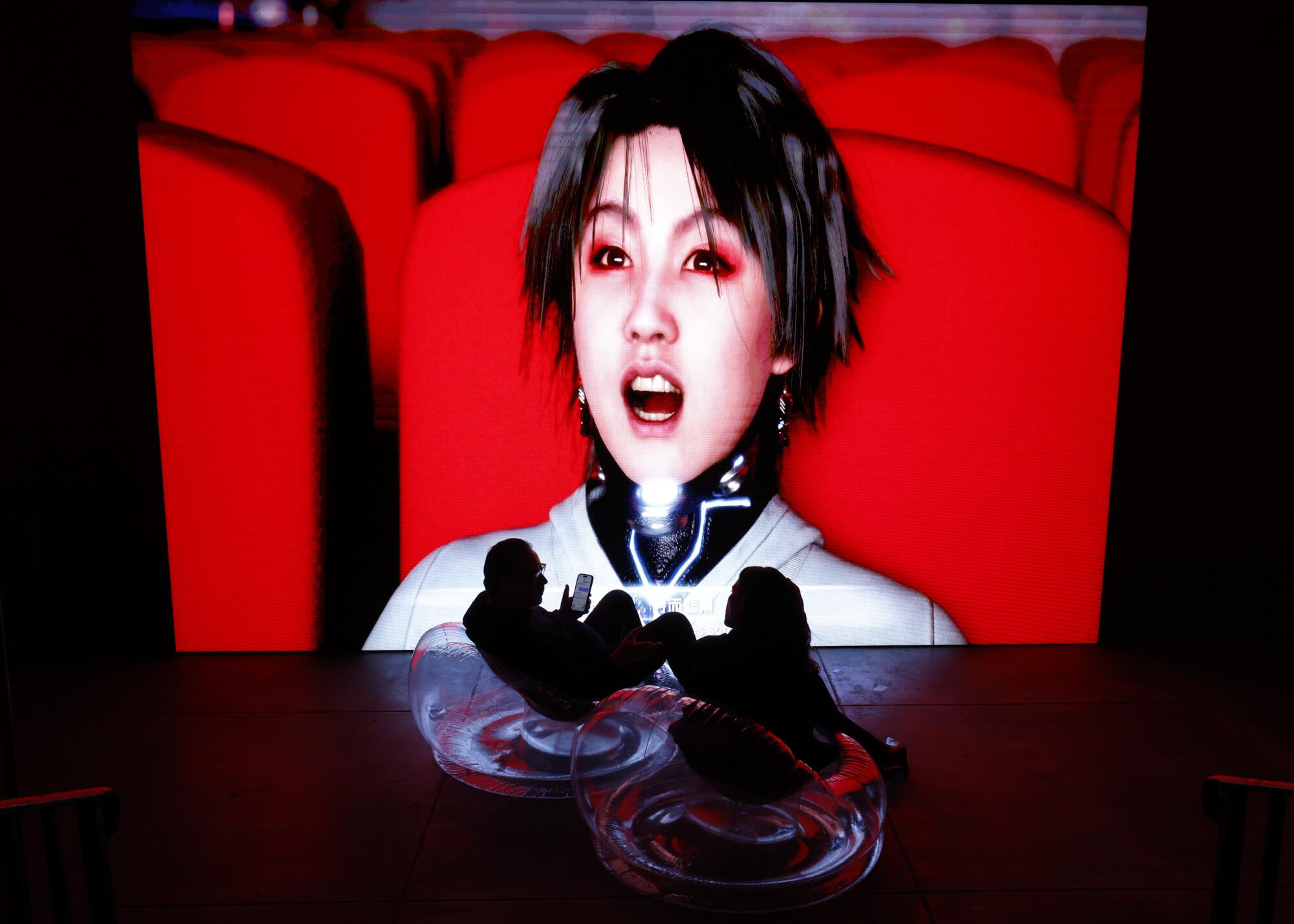 A man and a woman sit in front of a bright movie screen.