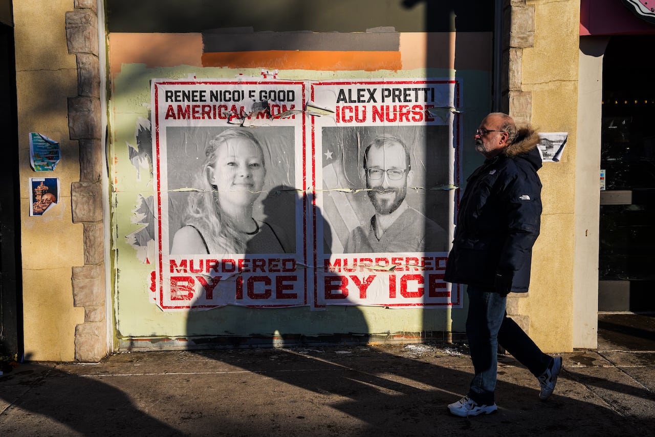 A man walks by posters of Renee Nicole Good and Alex Pretti, who were both fatally shot by federal agents, in Minneapolis, Saturday, Jan. 31, 2026.