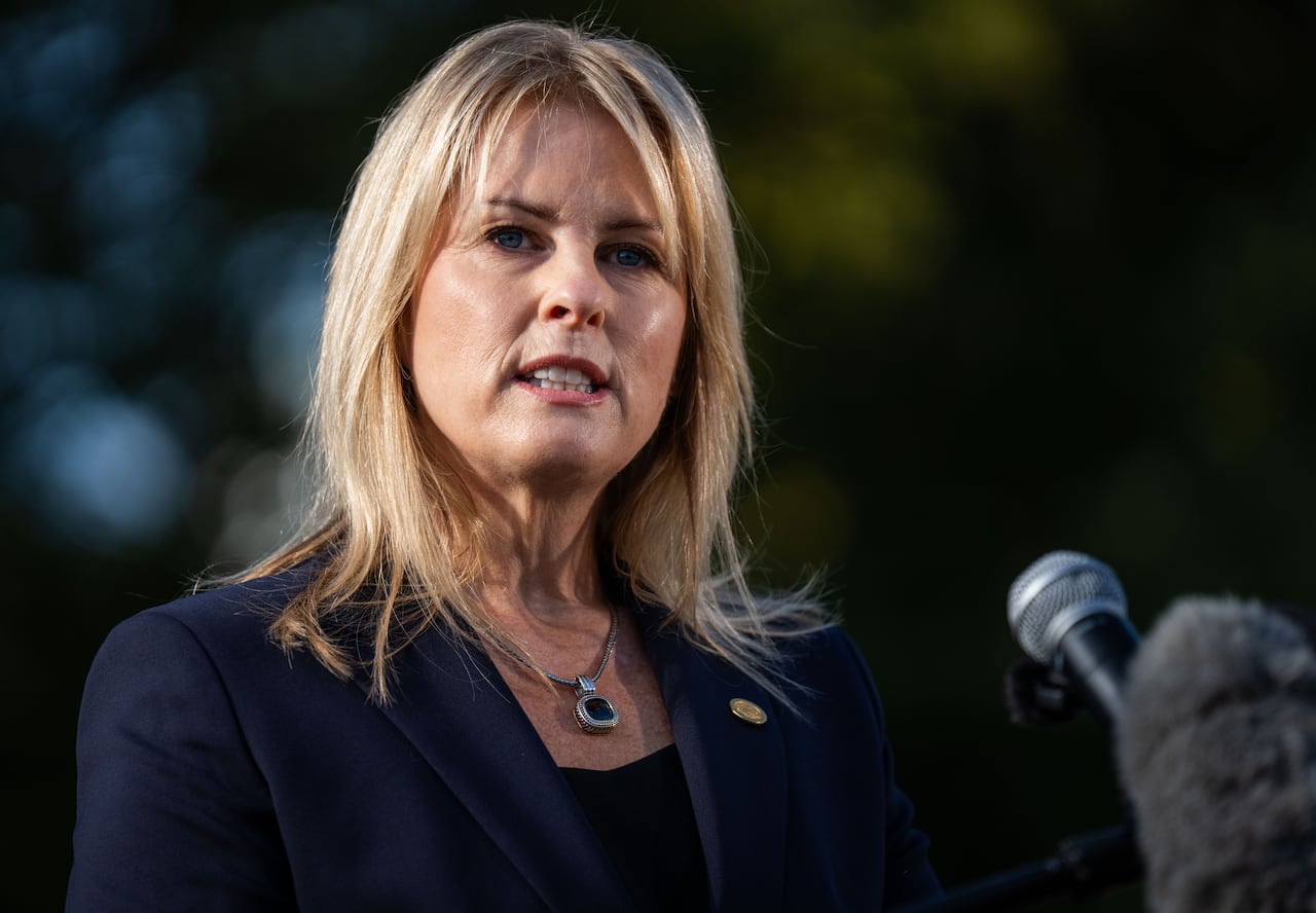 A woman with blonde hair wearing a suit speaks at a microphone