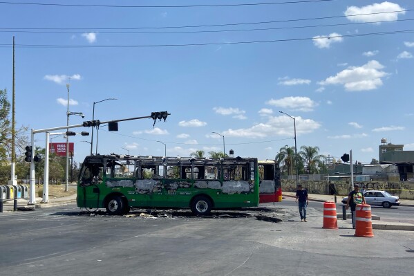 Pedestrians walk past charred buses that were set on fire, on a road in Guadalajara, Jalisco state, Mexico, Sunday, Feb. 22, 2026, after the death of the leader of the Jalisco New Generation Cartel, Nemesio Rubén Oseguera Cervantes, known as "El Mencho." (AP Photo/Refugio Ruiz)
