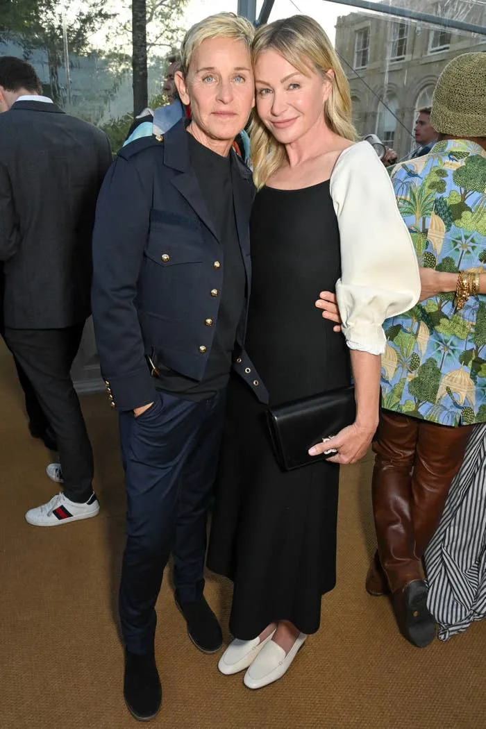 Ellen DeGeneres with an arm around Portia de Rossi's waist as they pose at an event with others in the background