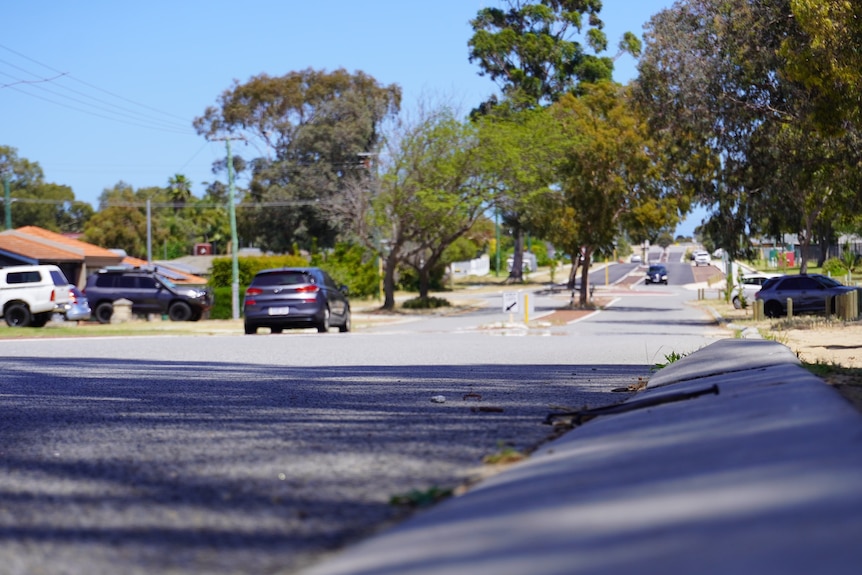 A suburban street with a kerb in the foreground and cars parked on the left