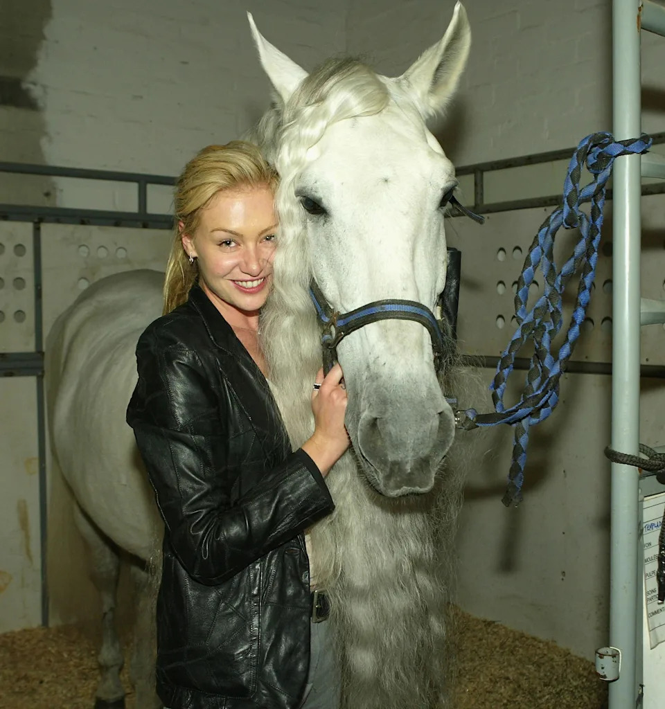 Portia de Rossi smiling next to a horse in a stable, wearing a leather jacket