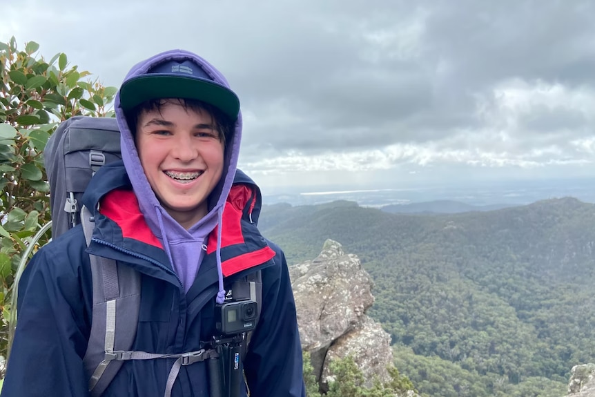 Boy wearing hood and cap and hiking bag on top of a mountain.