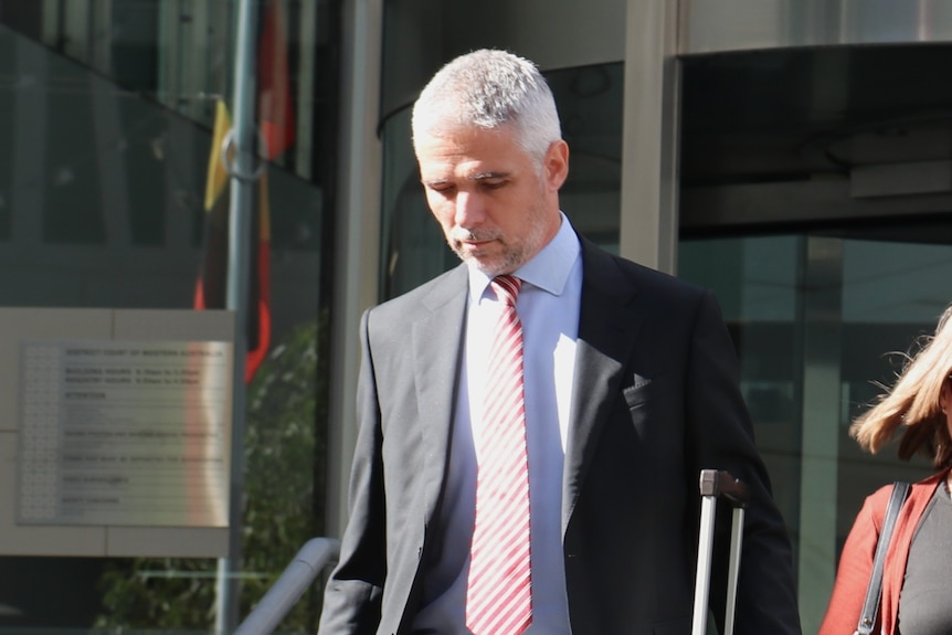 Ben Stanwix walks down a flight of stairs outdoors while wearing a suit.