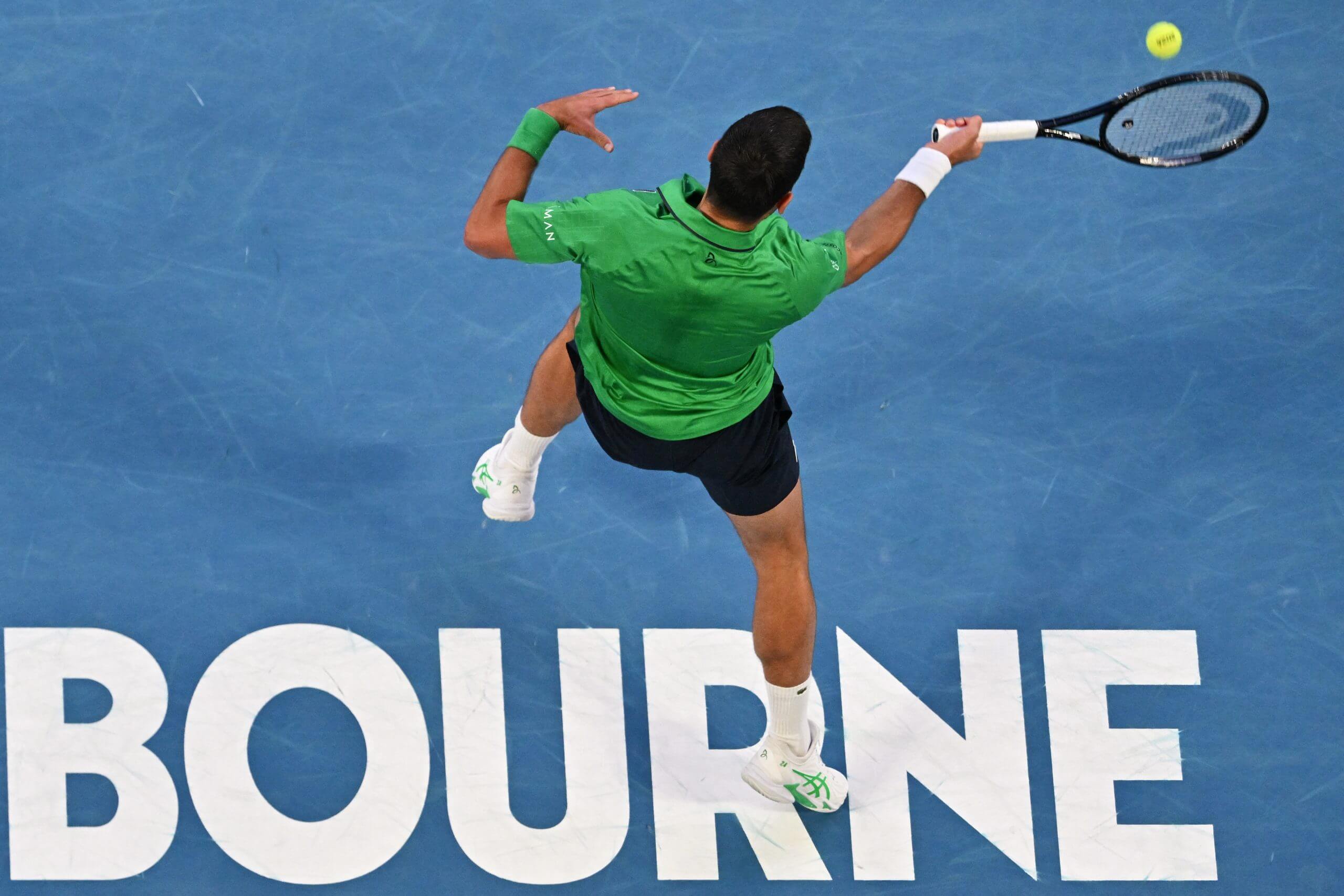Novak Djokovic hits a forehand standing on a blue court with the word MELBOURNE written in all-white capital letters.