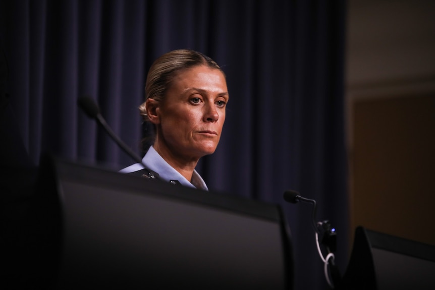 A police officer stands behind a lecturn with a curtain backdrop