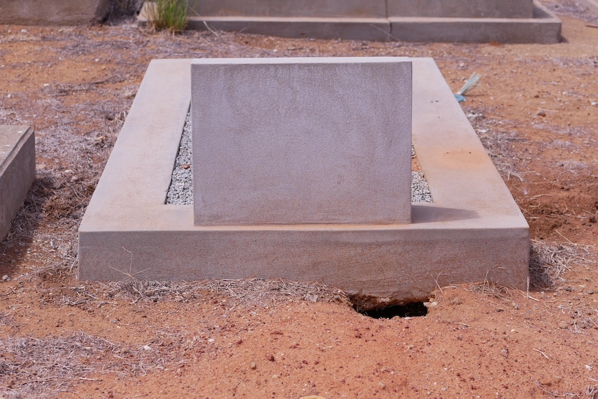A picture of a grave, with a rabbit burrow in the corner.