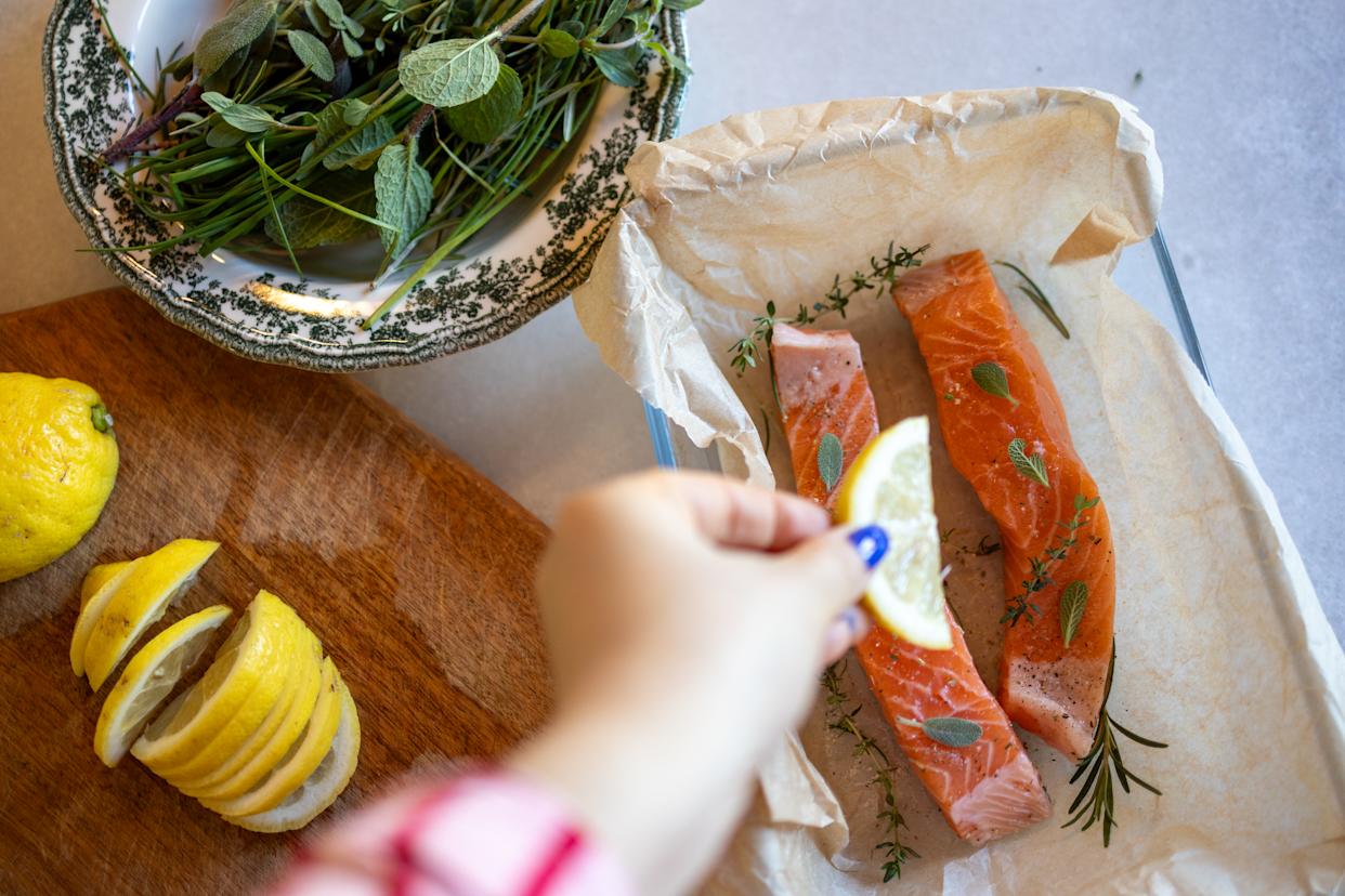 High angel view of raw salmon steaks decorated with different herbs and slices of lemon before baking. Some salmon cooking ingredients, such as lime, salt, pepper, different herbs, rosemary are visible by side. Preparing food at home. Homemade