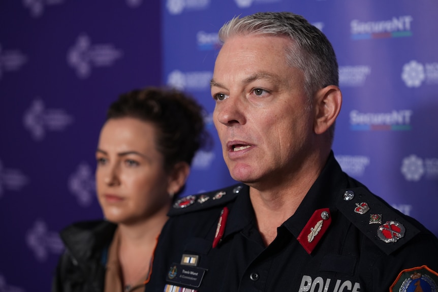 A police official speaking to media, a woman is standing nearby.