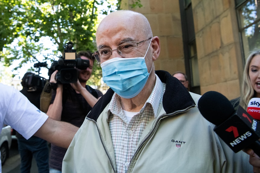 Mr Obeid wearing a mask with reporters and microphonesa round him.