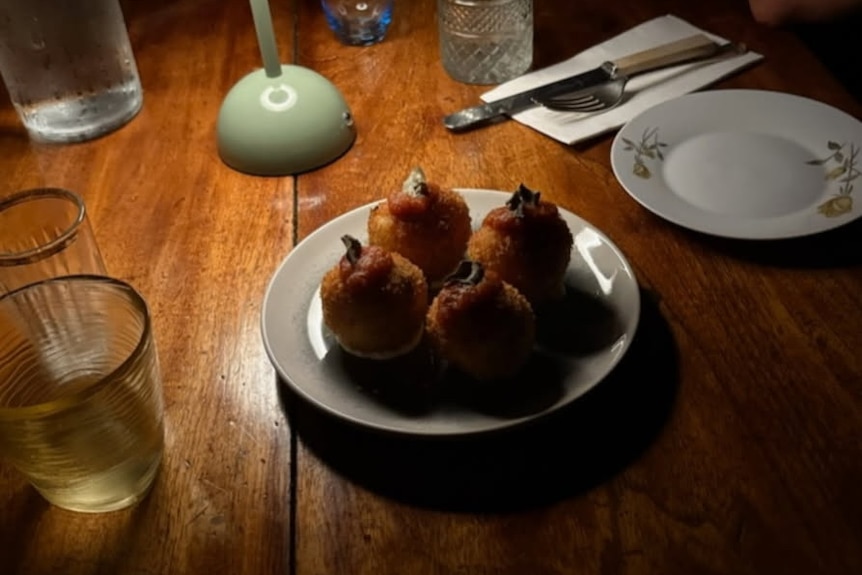Lamp lighting up wooden table with four arancinis on a plate.