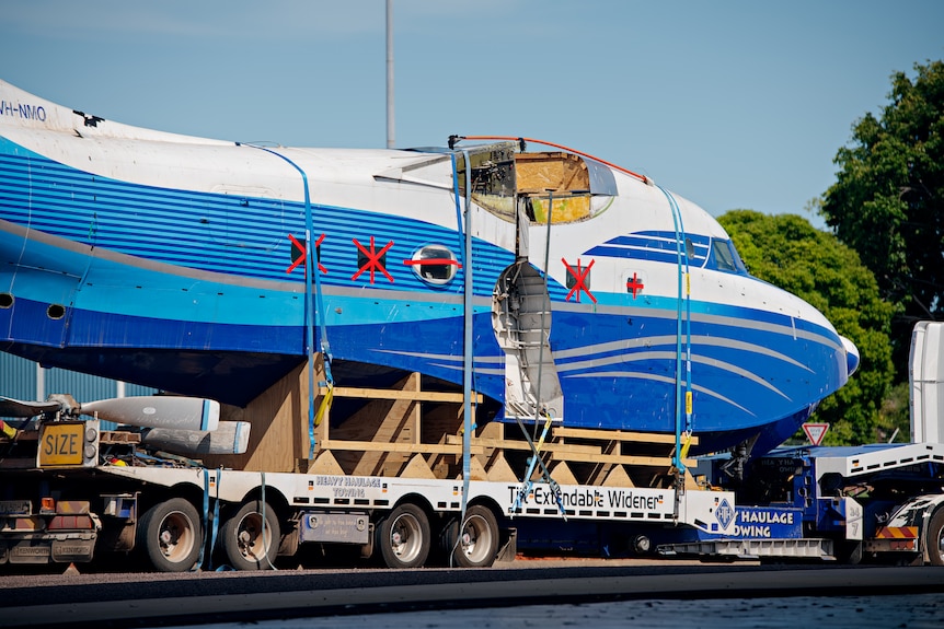 The exterior shell of a large, blue and white aeroplane, with red tape over the windows.