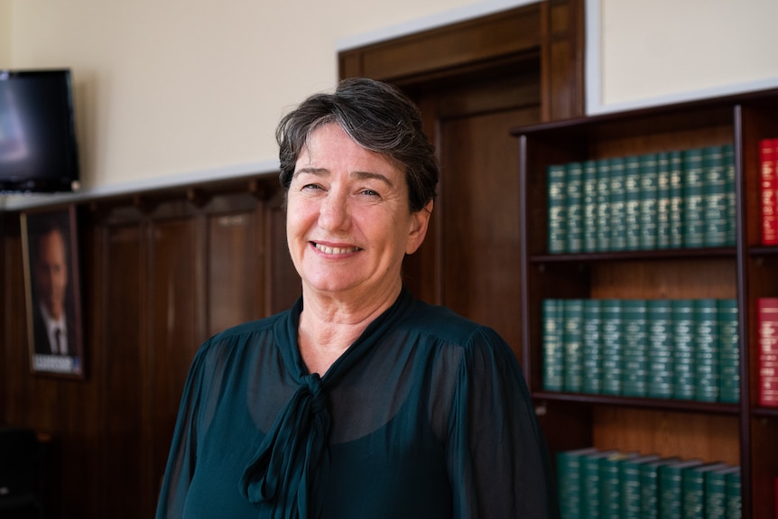 A woman stands in front of a bookcase, smiling.