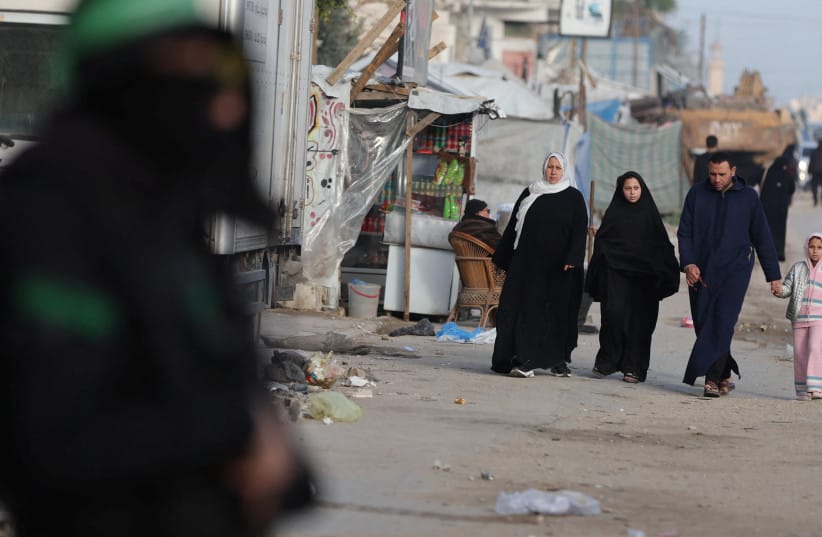 A Hamas terorrist stands guard as Palestinians walk on a street during Eid al-Fitr, in Gaza City, March 20, 2026.
