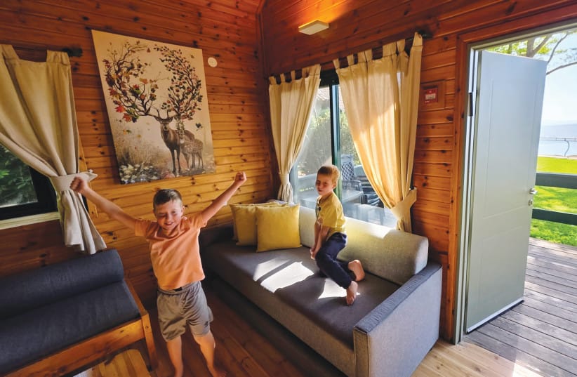 Inside the family cabin: The inviting timber interior reveals a thoughtful multi-level design featuring an attic loft for children, while the open doorway frames a direct view of green lawns and the shimmering lake outside.