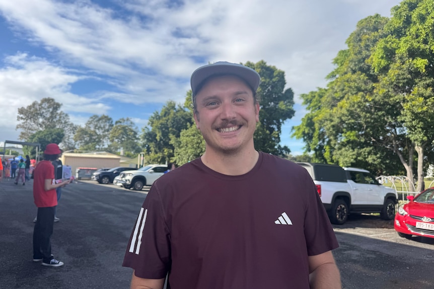 A man in a maroon shirt and hat smiling at the camera.