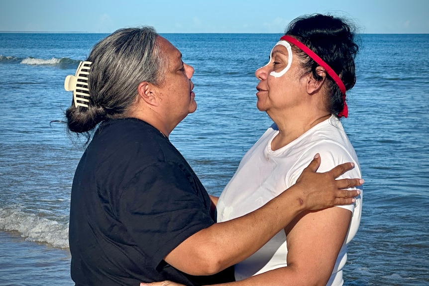 Two people standing in the water, holding one another with their eyes closed.