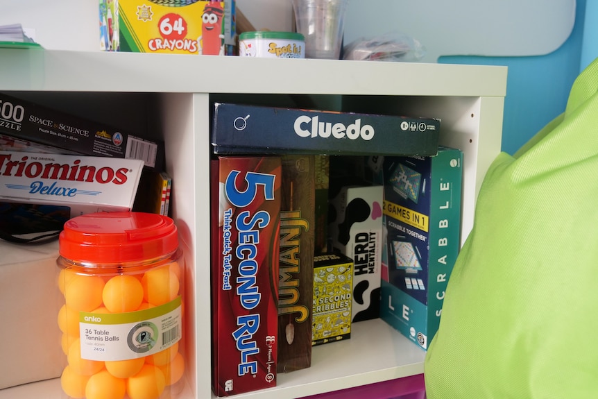 A white bookshelf filled with board games like cluedo, jumanji and scrabble.